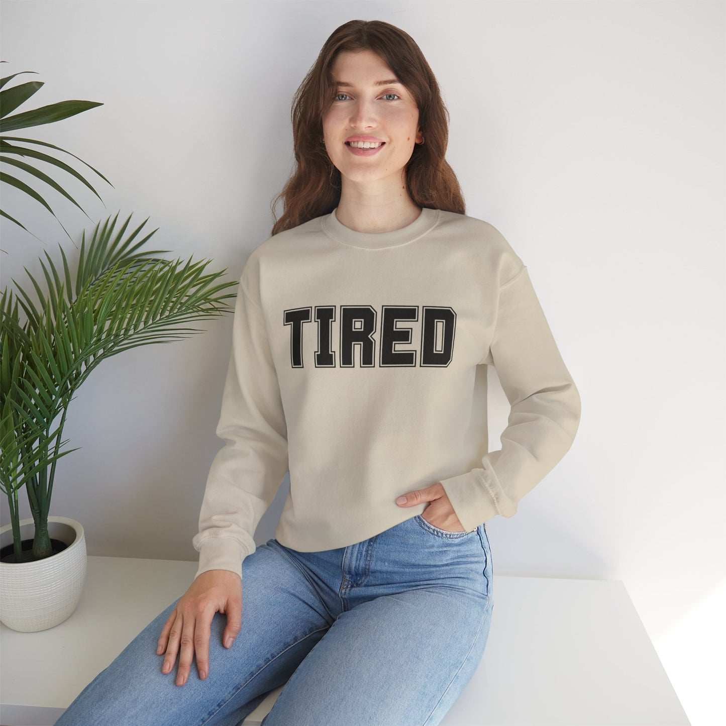 Model wearing grey “Tired” crewneck sitting on couch