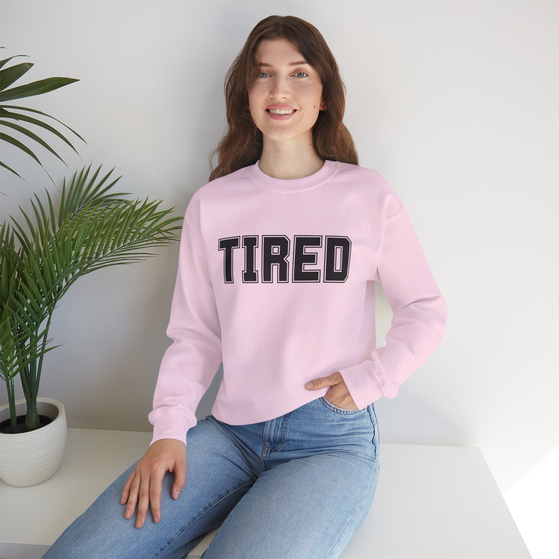 Model wearing pink “Tired” crewneck smiling indoors